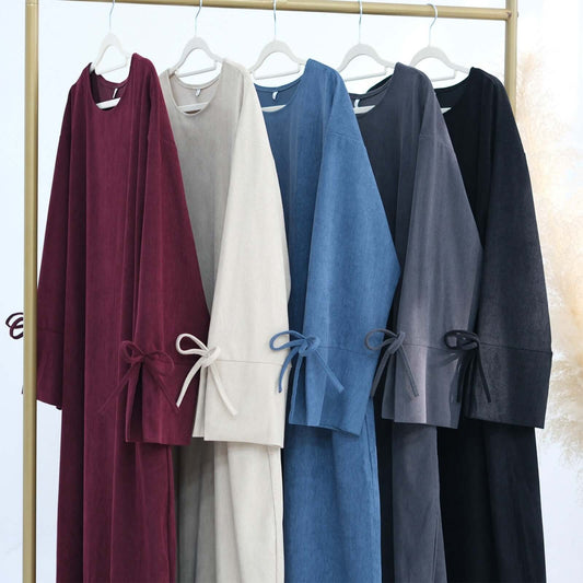 Nawal Corduroy Abaya collection featuring various colors on hangers, showcasing elegant design and adjustable ties.